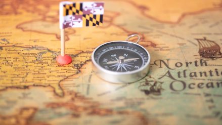 The flag of Maryland and the compass on the old world map. The concept of domestic tourism and recreation in America.