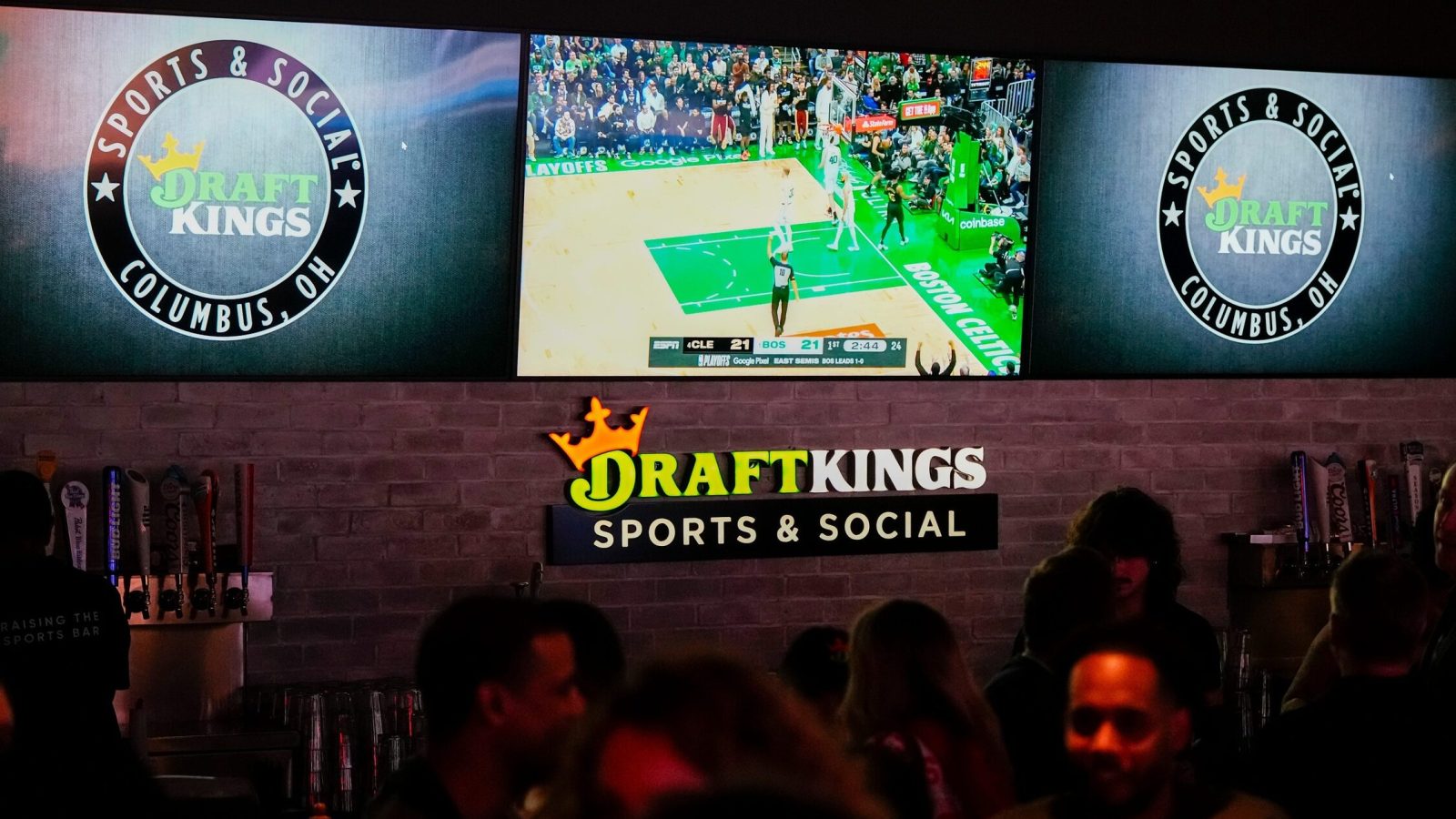 Sports are shown on TVs behind a bar as guests enjoy the grand opening of DraftKings Sports & Social in Ohio.