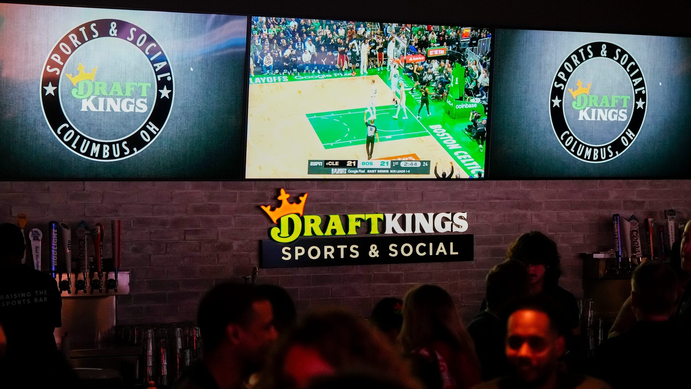 Sports are shown on TVs behind a bar as guests enjoy the grand opening of DraftKings Sports & Social in Ohio.