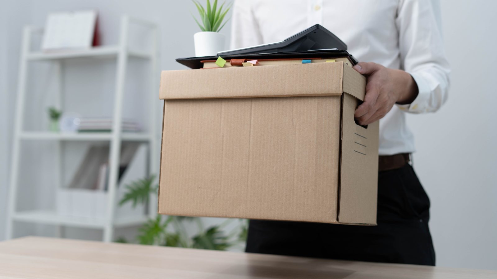 A businessman holds a box for personal items after sending a resignation letter to an executive or manager. Include information about resignation and vacancies and job changes.