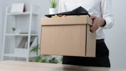 A businessman holds a box for personal items after sending a resignation letter to an executive or manager. Include information about resignation and vacancies and job changes.